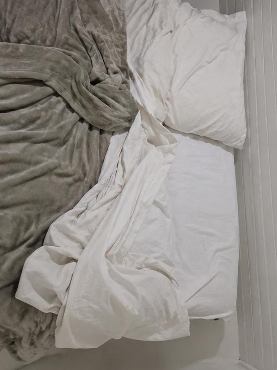 Bed linens before service, with sheets pulled loose, the duvet twisted and pillows out of position against the panelled wall