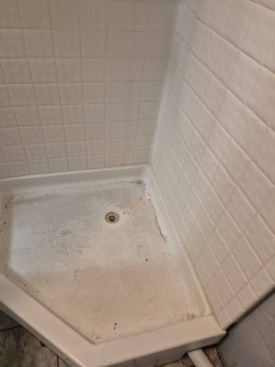 Shower pan before cleaning, with soil worked into the textured floor and dark debris along the caulk line at the wall