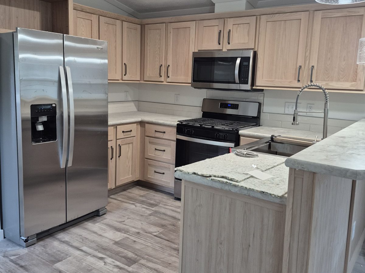 Kitchen with light oak cabinets, stainless steel appliances and a stone peninsula, counters clear and the floor clean