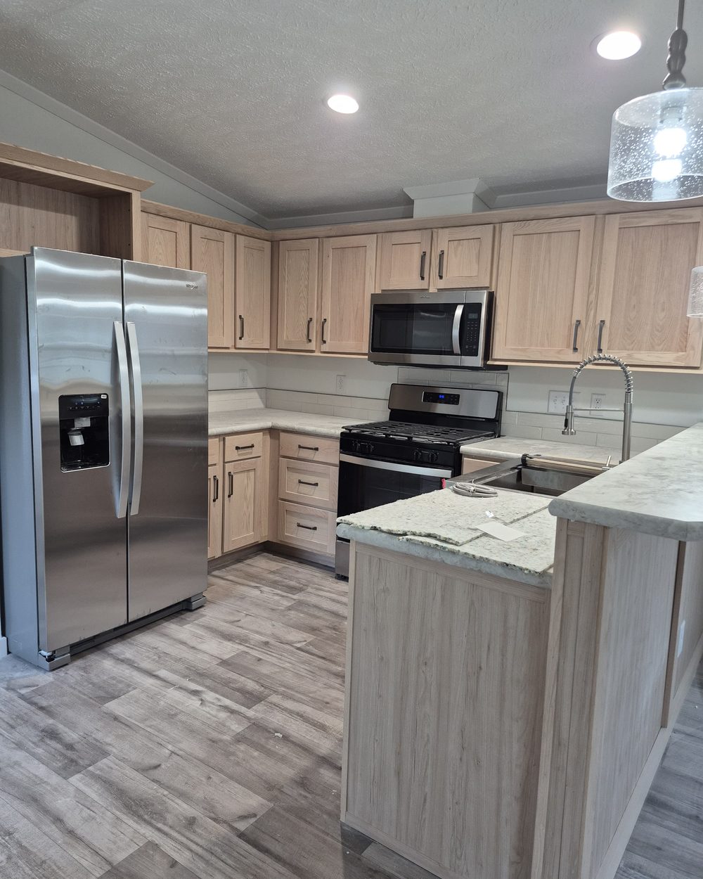 Kitchen with light oak cabinets, stainless steel appliances and a stone peninsula, counters clear and the floor clean