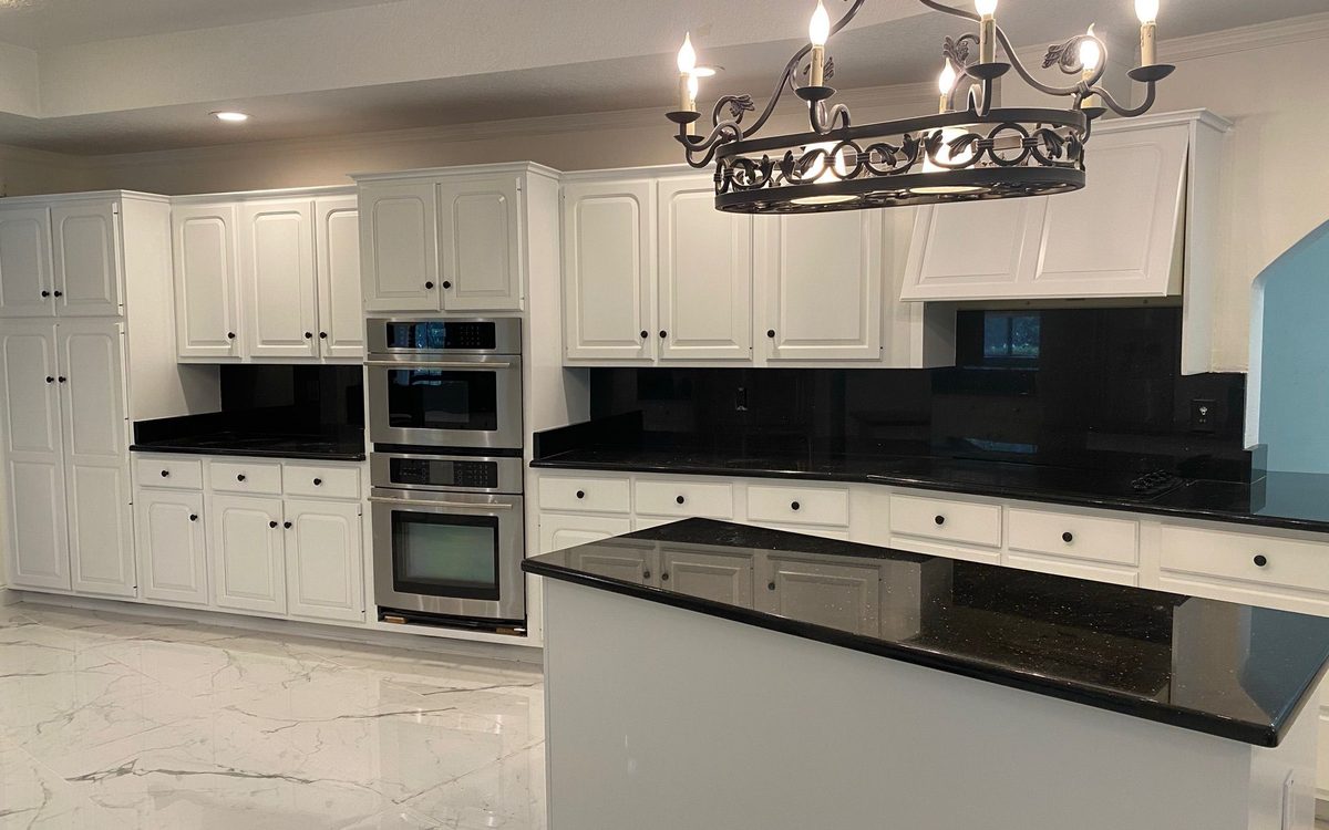 Large kitchen with white raised-panel cabinets, polished black granite counters and a wrought-iron chandelier