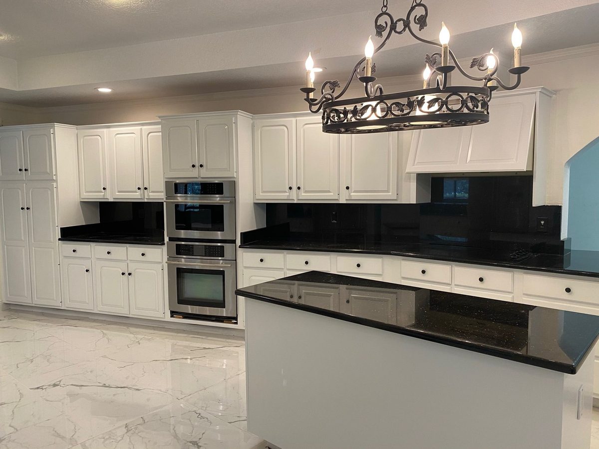 Large kitchen with white raised-panel cabinets, polished black granite counters and a wrought-iron chandelier