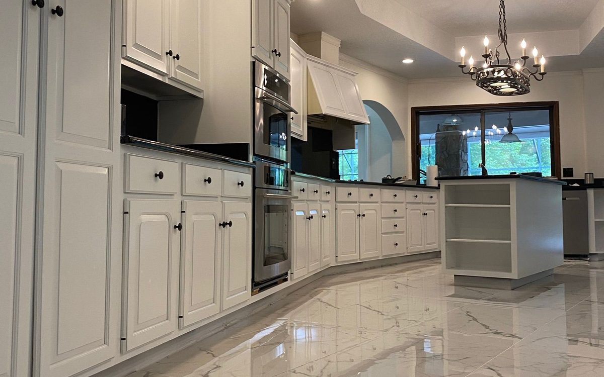 The same kitchen seen down its length, with white cabinetry, double wall ovens and a polished marble-look tile floor