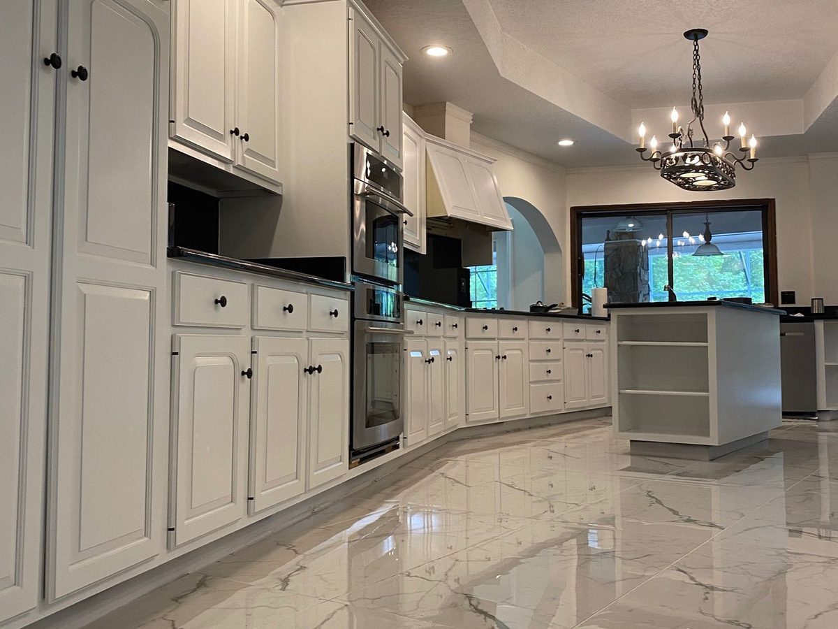 The same kitchen seen down its length, with white cabinetry, double wall ovens and a polished marble-look tile floor