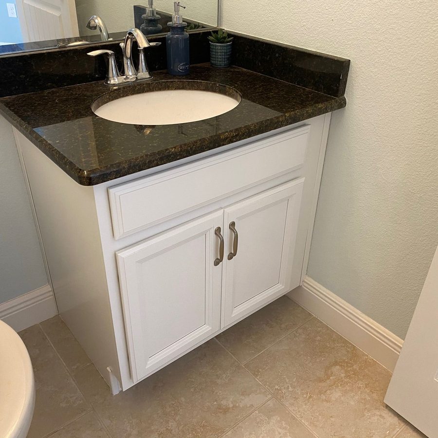 Small bathroom vanity with a white cabinet, dark granite top, chrome faucet and a clean tiled floor
