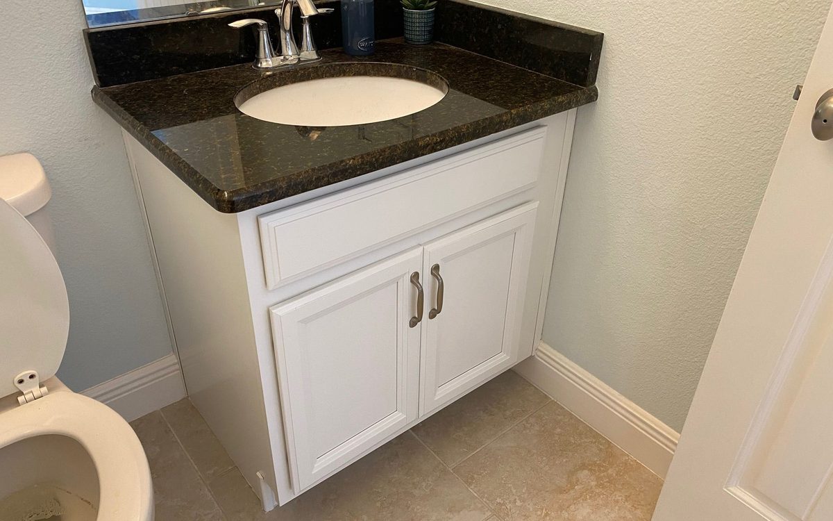 Small bathroom vanity with a white cabinet, dark granite top, chrome faucet and a clean tiled floor