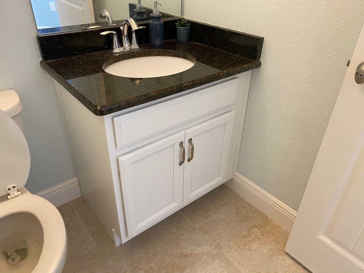 Small bathroom vanity with a white cabinet, dark granite top, chrome faucet and a clean tiled floor