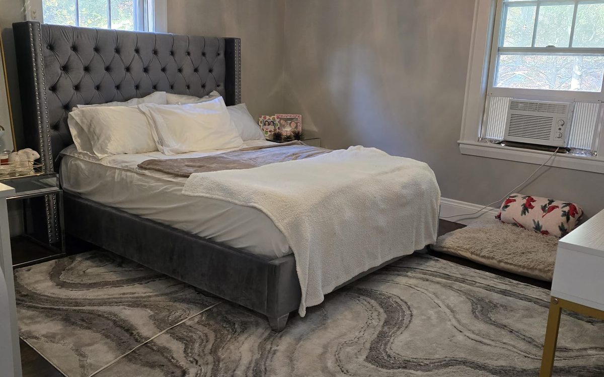 Bedroom with a grey tufted headboard, white bedding, a patterned rug and clear floor space