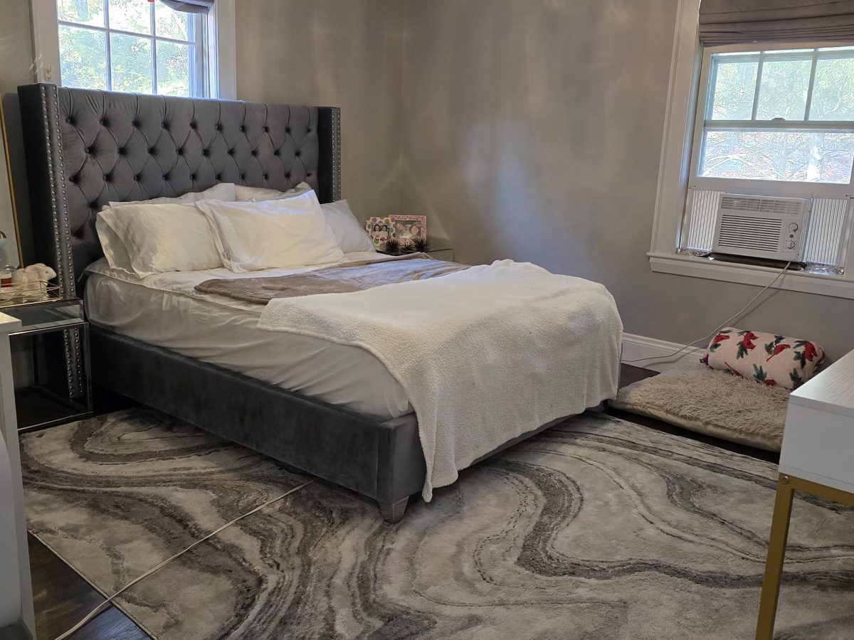 Bedroom with a grey tufted headboard, white bedding, a patterned rug and clear floor space