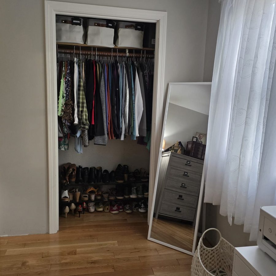Bedroom closet with clothes hung in order, two shoe racks and a floor mirror beside it