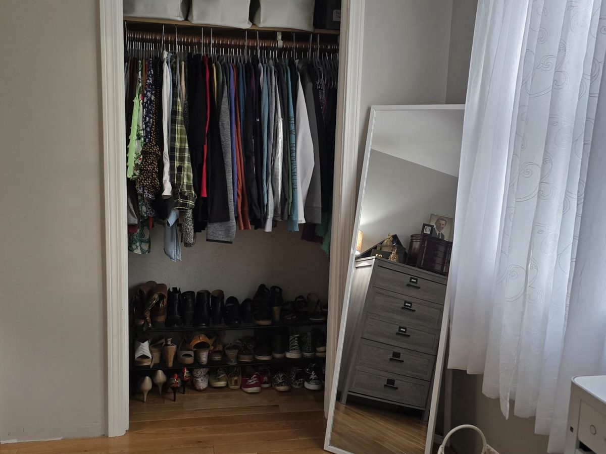 Bedroom closet with clothes hung in order, two shoe racks and a floor mirror beside it