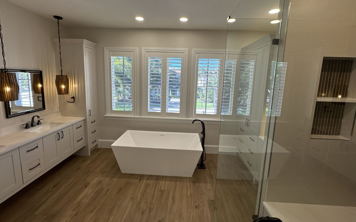 Large bathroom with a freestanding tub, plantation shutters, a glass shower enclosure and a wood-look floor