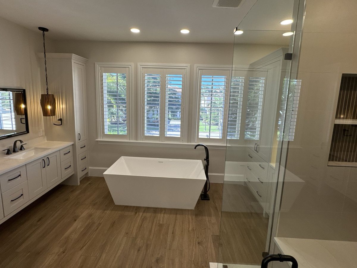 Large bathroom with a freestanding tub, plantation shutters, a glass shower enclosure and a wood-look floor