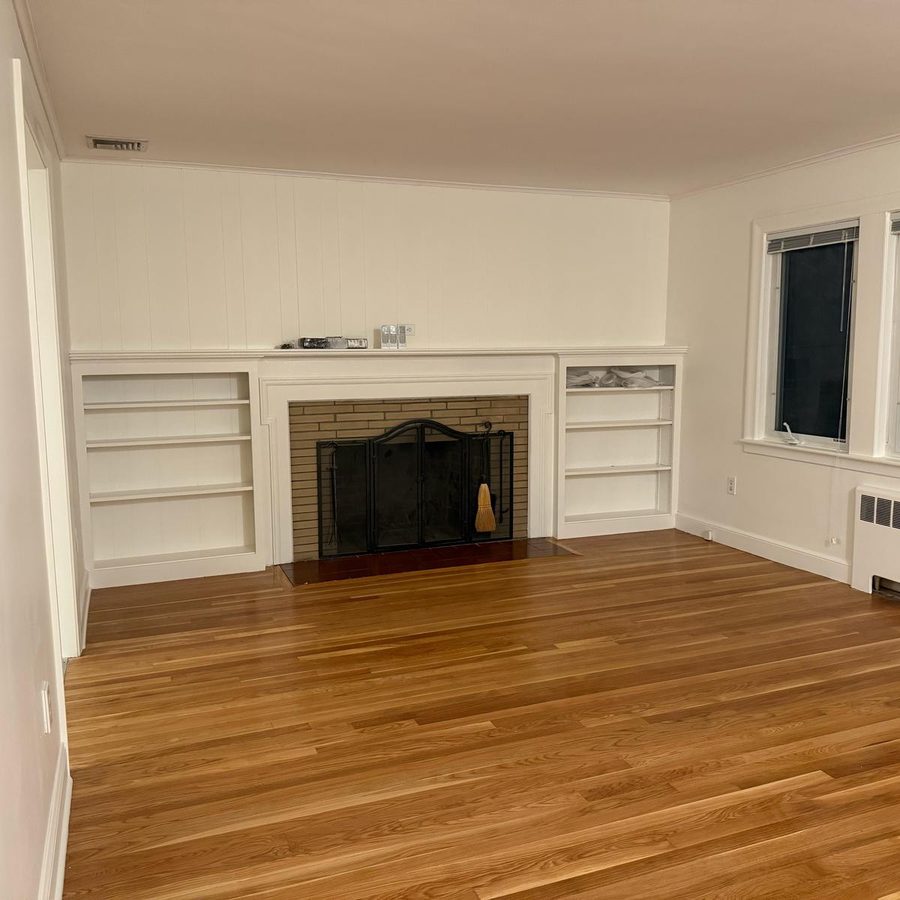 Empty living room with a white fireplace, built-in shelves and a bare hardwood floor