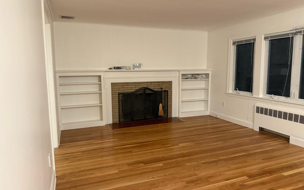 Empty living room with a white fireplace, built-in shelves and a bare hardwood floor
