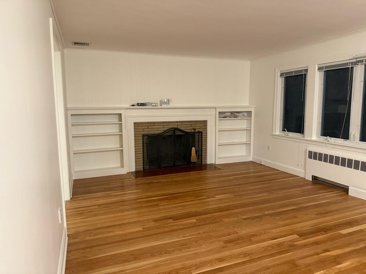 Empty living room with a white fireplace, built-in shelves and a bare hardwood floor